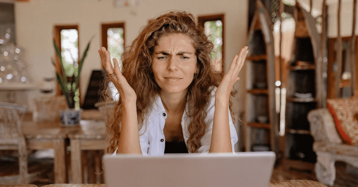 An image of a person sitting at a computer with her hands in her hair and looks frustrated