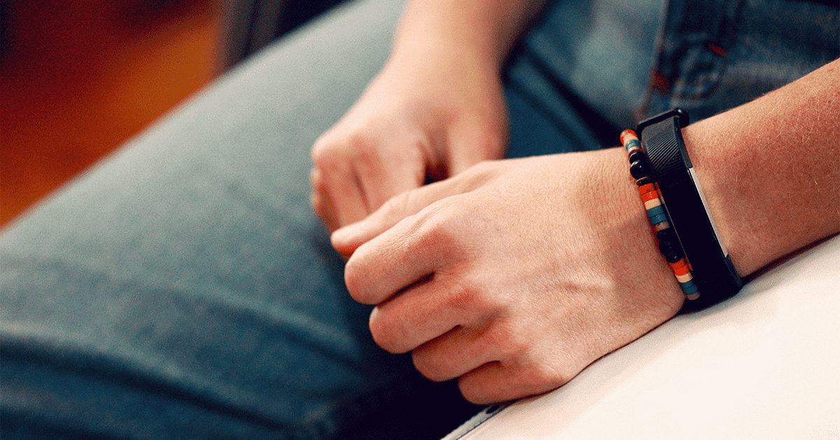 a photo of clasped hands in a lap, the person is wearing a small rainbow bracelet