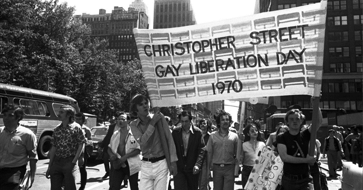 A black and white photograph of a parade and people holding a sign that says 'Christopher Street Liberation Day 1970'